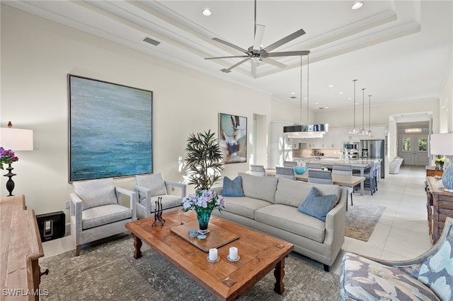 tiled living room with a raised ceiling, ceiling fan, and crown molding