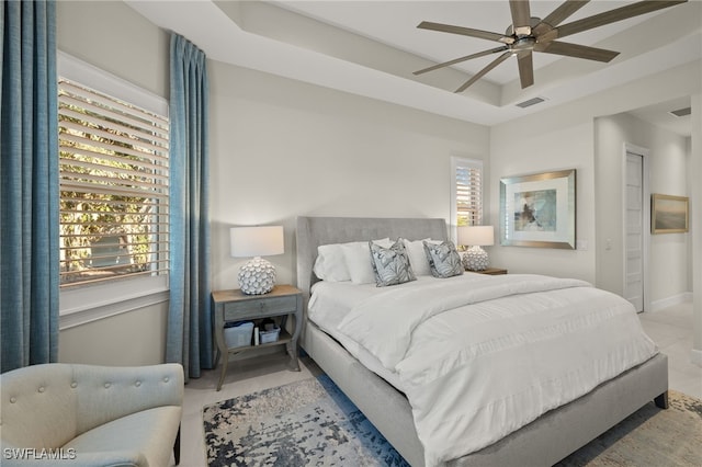 bedroom featuring multiple windows, a raised ceiling, and ceiling fan