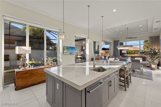 kitchen featuring sink, gray cabinetry, a tray ceiling, pendant lighting, and a kitchen island with sink