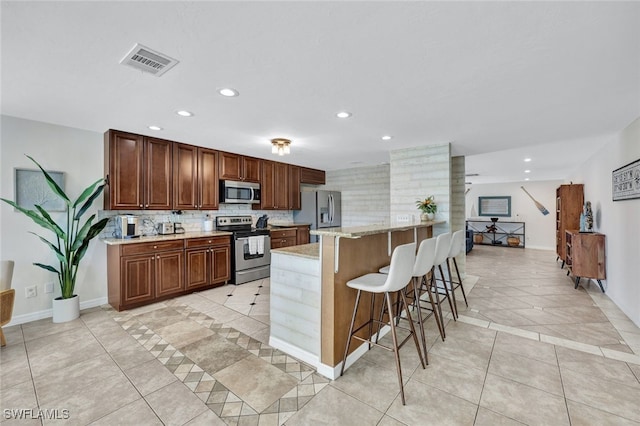 kitchen featuring light stone countertops, stainless steel appliances, decorative backsplash, a breakfast bar, and light tile patterned flooring