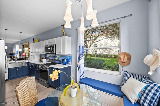 kitchen with electric range, light wood-style floors, blue cabinetry, stainless steel microwave, and pendant lighting