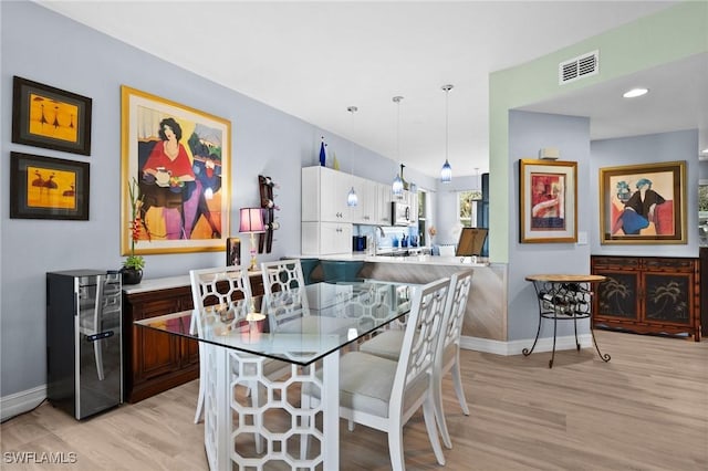 dining area featuring light wood finished floors, wine cooler, visible vents, and baseboards