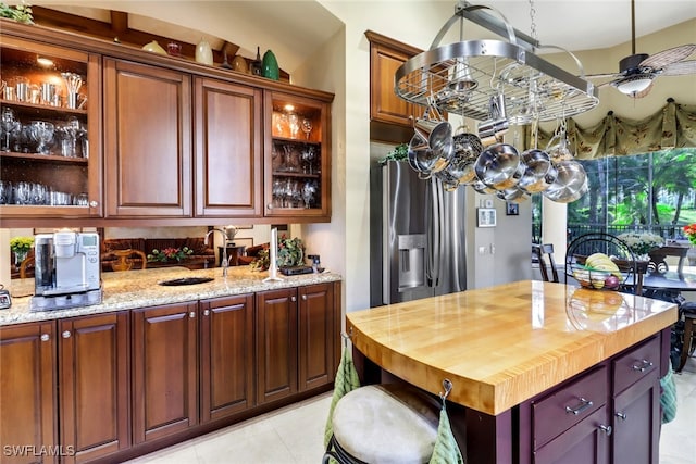 kitchen with ceiling fan, sink, stainless steel fridge with ice dispenser, light stone counters, and light tile patterned flooring