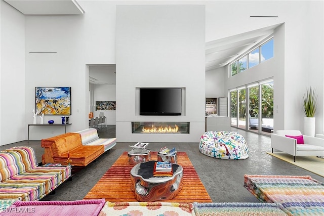 living area featuring a towering ceiling and a glass covered fireplace