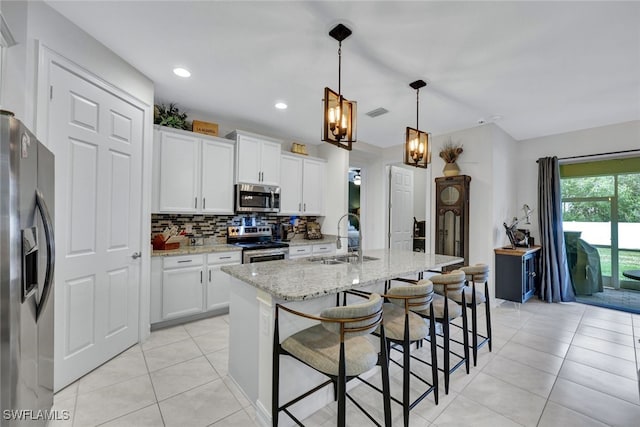 kitchen featuring stainless steel appliances, sink, white cabinetry, light stone counters, and a center island with sink