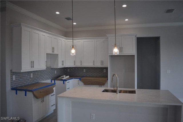 kitchen with decorative light fixtures, white cabinetry, and a kitchen island with sink