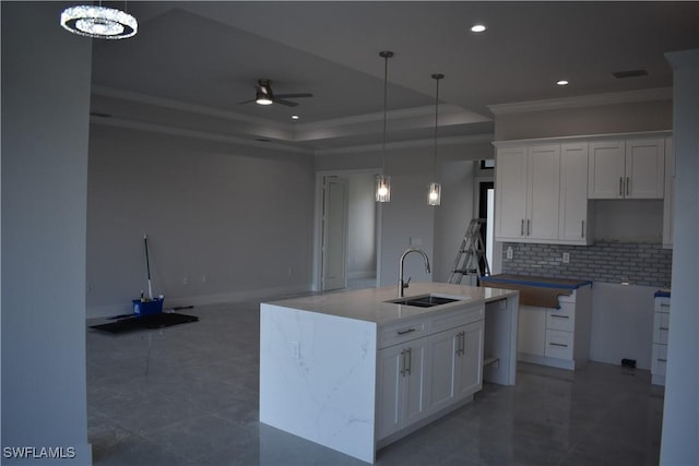 kitchen featuring backsplash, ceiling fan with notable chandelier, sink, a center island with sink, and white cabinetry