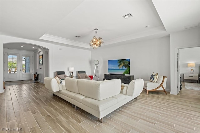 living room featuring a tray ceiling, crown molding, french doors, and an inviting chandelier