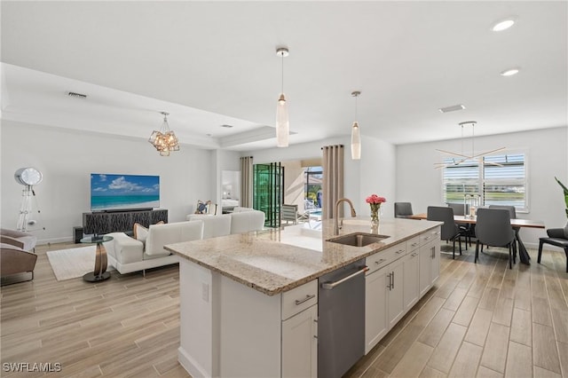 kitchen featuring white cabinets, sink, hanging light fixtures, an island with sink, and light stone counters