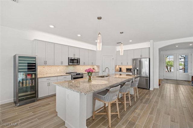 kitchen with sink, beverage cooler, an island with sink, white cabinets, and appliances with stainless steel finishes