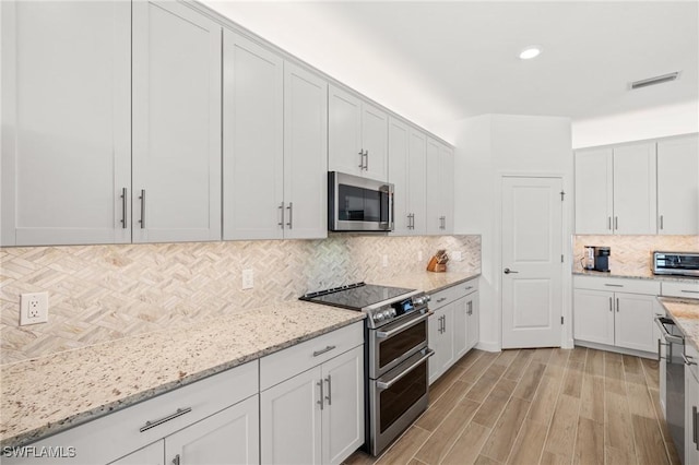 kitchen featuring white cabinetry, stainless steel appliances, light stone counters, decorative backsplash, and light wood-type flooring