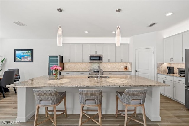 kitchen featuring decorative backsplash, decorative light fixtures, a center island with sink, and light stone counters