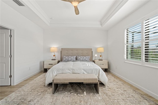 bedroom with light wood-type flooring, a tray ceiling, ceiling fan, and crown molding