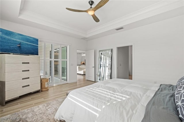 bedroom with ceiling fan, light hardwood / wood-style floors, a raised ceiling, and ornamental molding