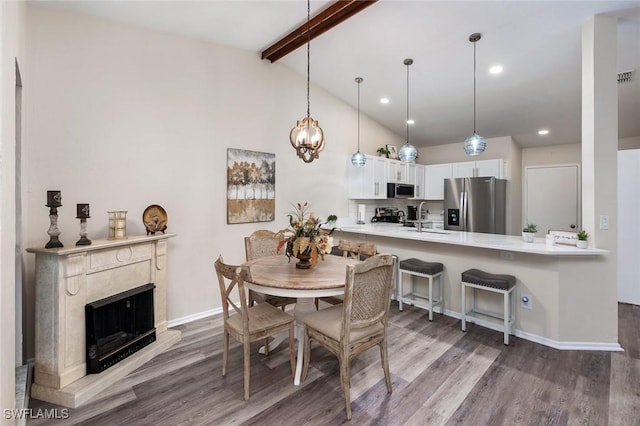 dining area with a fireplace, sink, wood-type flooring, and vaulted ceiling with beams