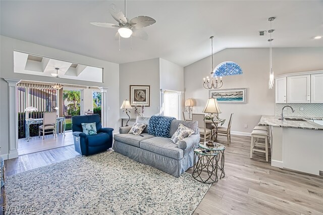 living room featuring light wood-type flooring, ceiling fan with notable chandelier, vaulted ceiling, and sink