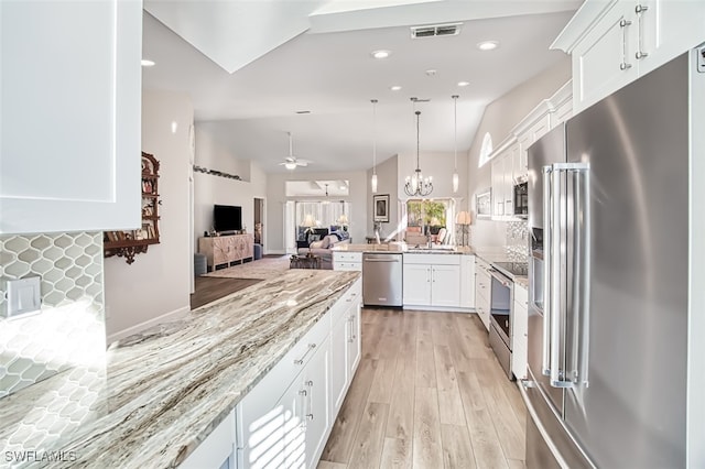 kitchen featuring appliances with stainless steel finishes, tasteful backsplash, ceiling fan with notable chandelier, vaulted ceiling, and white cabinetry