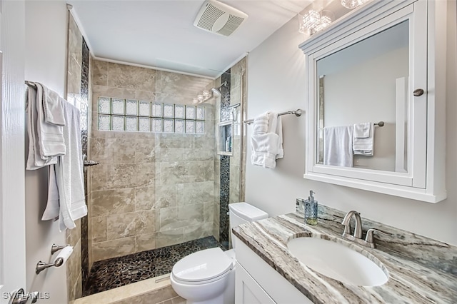 bathroom featuring a tile shower, vanity, and toilet