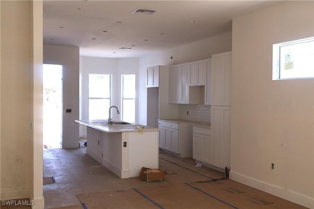 kitchen featuring backsplash, a center island with sink, white cabinetry, and sink