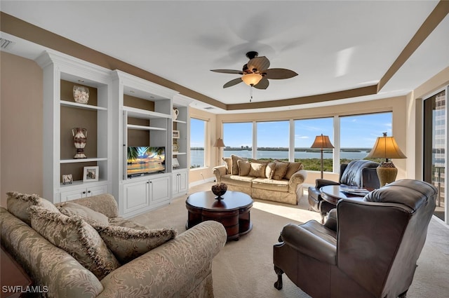 living room featuring light colored carpet, built in features, ceiling fan, and a tray ceiling