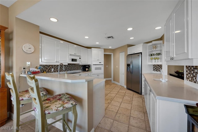 kitchen featuring a breakfast bar, white cabinetry, white appliances, and kitchen peninsula