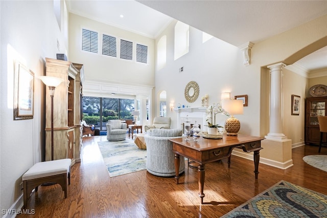 living room with ornate columns, hardwood / wood-style floors, a towering ceiling, and ornamental molding