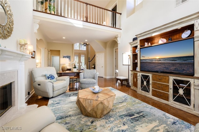 living room featuring wood-type flooring, a towering ceiling, and a premium fireplace