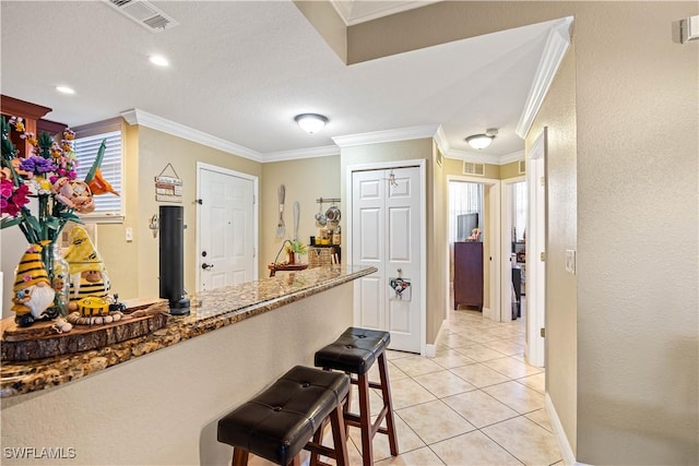 kitchen with a breakfast bar, stone countertops, crown molding, and light tile patterned flooring