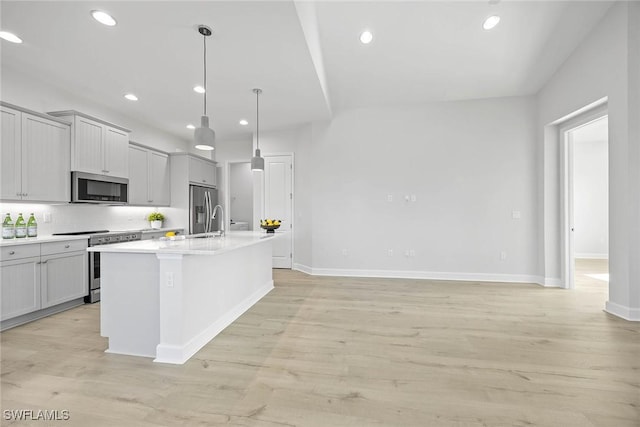 kitchen with hanging light fixtures, stainless steel appliances, light hardwood / wood-style floors, gray cabinets, and a kitchen island with sink