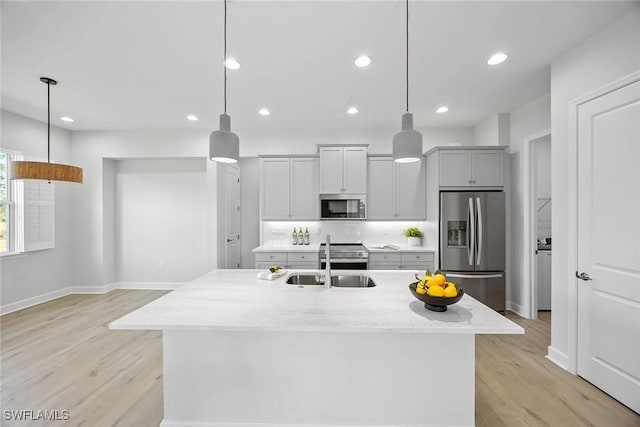 kitchen featuring pendant lighting, a center island with sink, sink, light stone counters, and stainless steel appliances