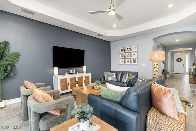 living room with a tray ceiling, ceiling fan, and hardwood / wood-style floors