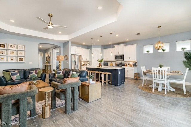 living room featuring ceiling fan with notable chandelier and a tray ceiling