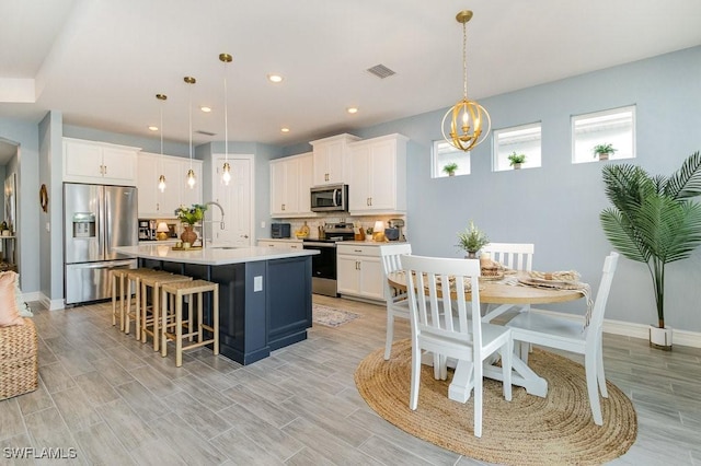 kitchen featuring white cabinetry, hanging light fixtures, stainless steel appliances, decorative backsplash, and a center island with sink