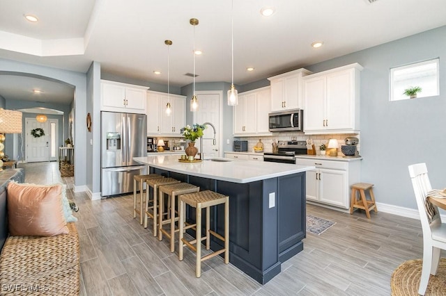 kitchen featuring white cabinets, pendant lighting, a center island with sink, and stainless steel appliances