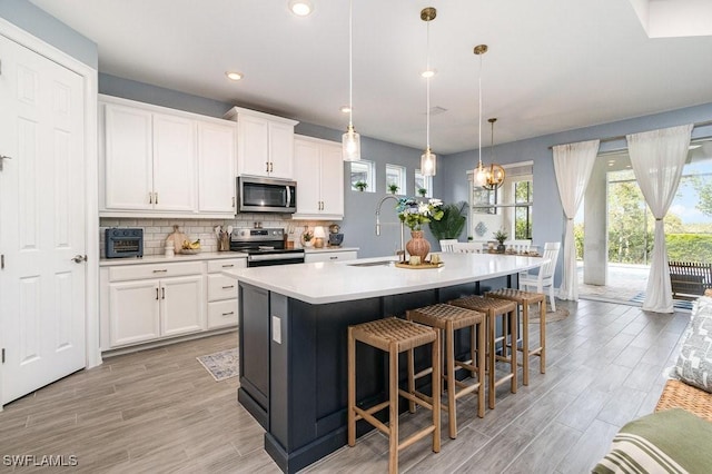 kitchen featuring a kitchen island with sink, white cabinets, hanging light fixtures, sink, and stainless steel appliances