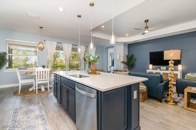 kitchen featuring a tray ceiling, ceiling fan, a kitchen island with sink, sink, and decorative light fixtures