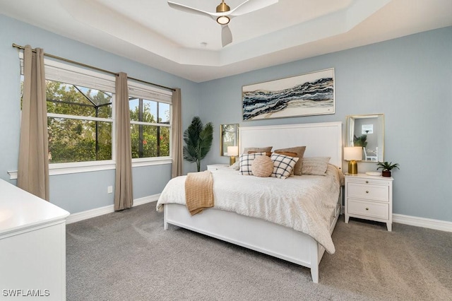 bedroom featuring ceiling fan, dark carpet, and a tray ceiling