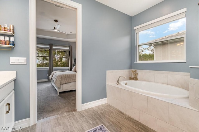 bathroom with tiled tub, ceiling fan, vanity, and a healthy amount of sunlight