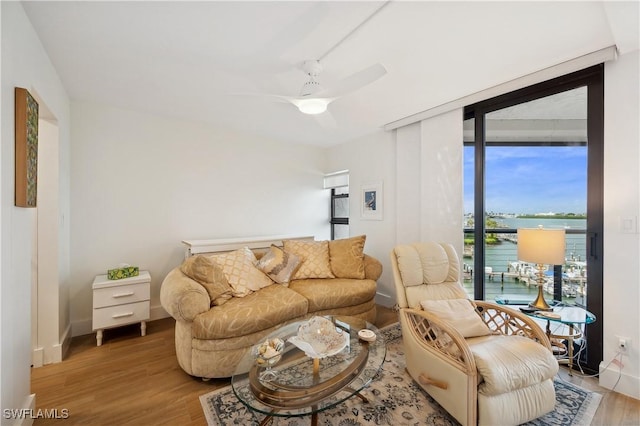 living room featuring ceiling fan, floor to ceiling windows, a water view, and wood-type flooring