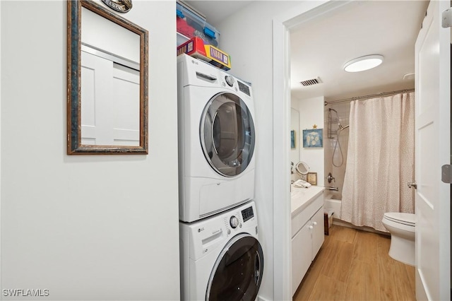 clothes washing area with light hardwood / wood-style flooring and stacked washer / dryer