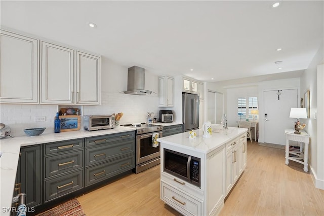 kitchen with tasteful backsplash, white cabinets, wall chimney range hood, and appliances with stainless steel finishes