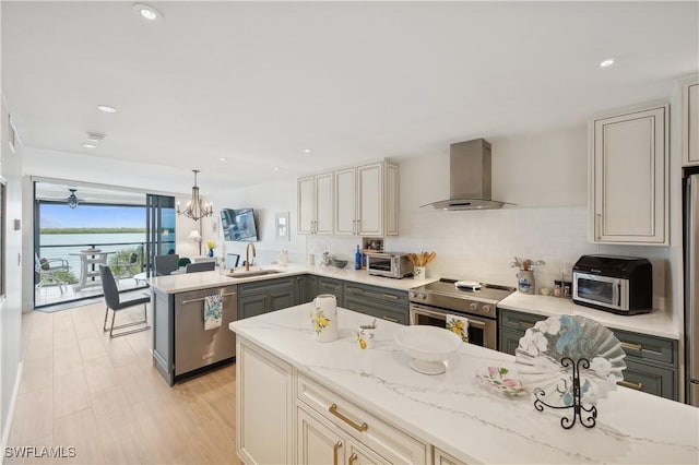 kitchen featuring gray cabinetry, wall chimney range hood, sink, decorative light fixtures, and stainless steel appliances