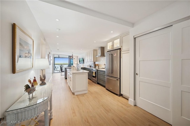 kitchen with a center island, wall chimney range hood, light hardwood / wood-style floors, white cabinetry, and stainless steel appliances