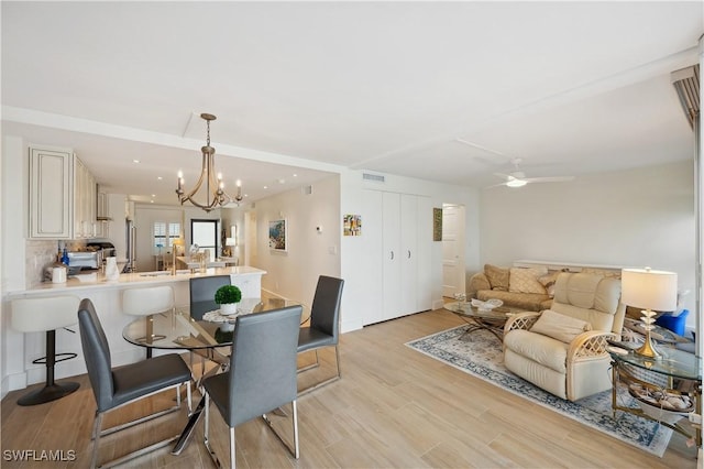 dining space featuring ceiling fan with notable chandelier and light wood-type flooring