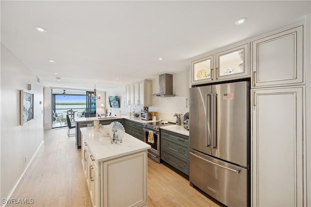 kitchen with light stone countertops, hanging light fixtures, wall chimney range hood, kitchen peninsula, and appliances with stainless steel finishes