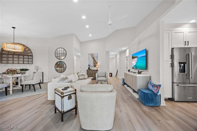 living room featuring ceiling fan, a towering ceiling, and light wood-type flooring