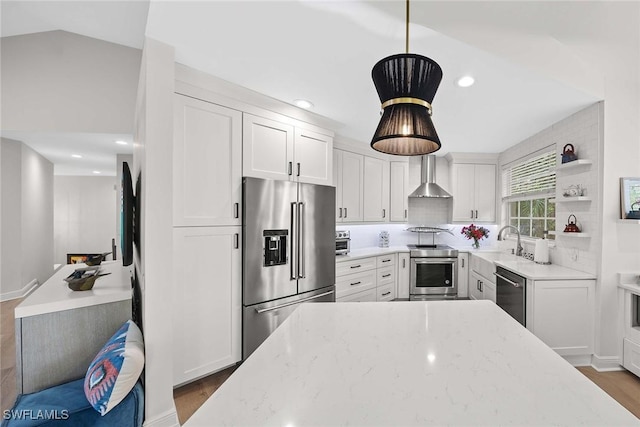 kitchen with white cabinets, wall chimney exhaust hood, hanging light fixtures, and appliances with stainless steel finishes