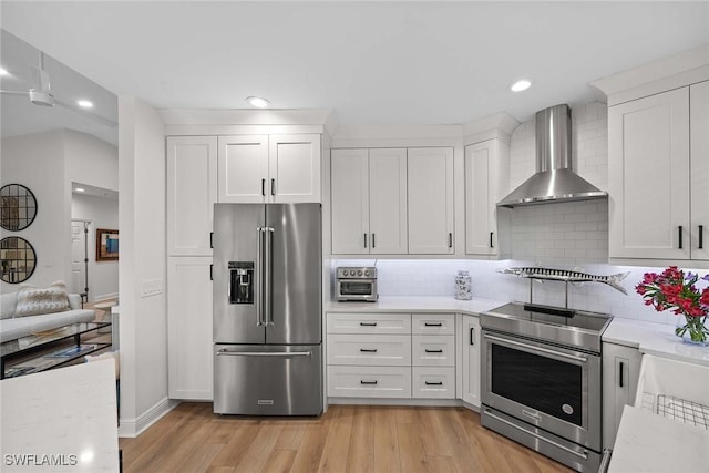 kitchen featuring backsplash, white cabinets, stainless steel appliances, and wall chimney range hood