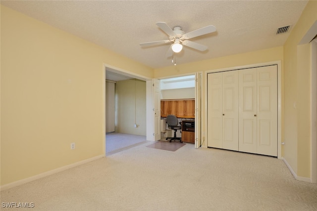 unfurnished bedroom with ceiling fan, a closet, light colored carpet, and a textured ceiling