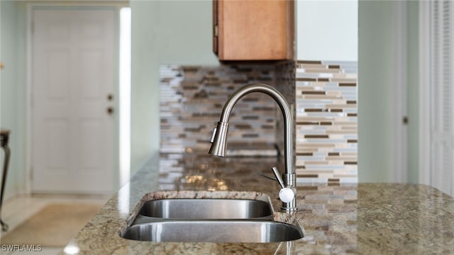 room details featuring sink, decorative backsplash, and light stone countertops